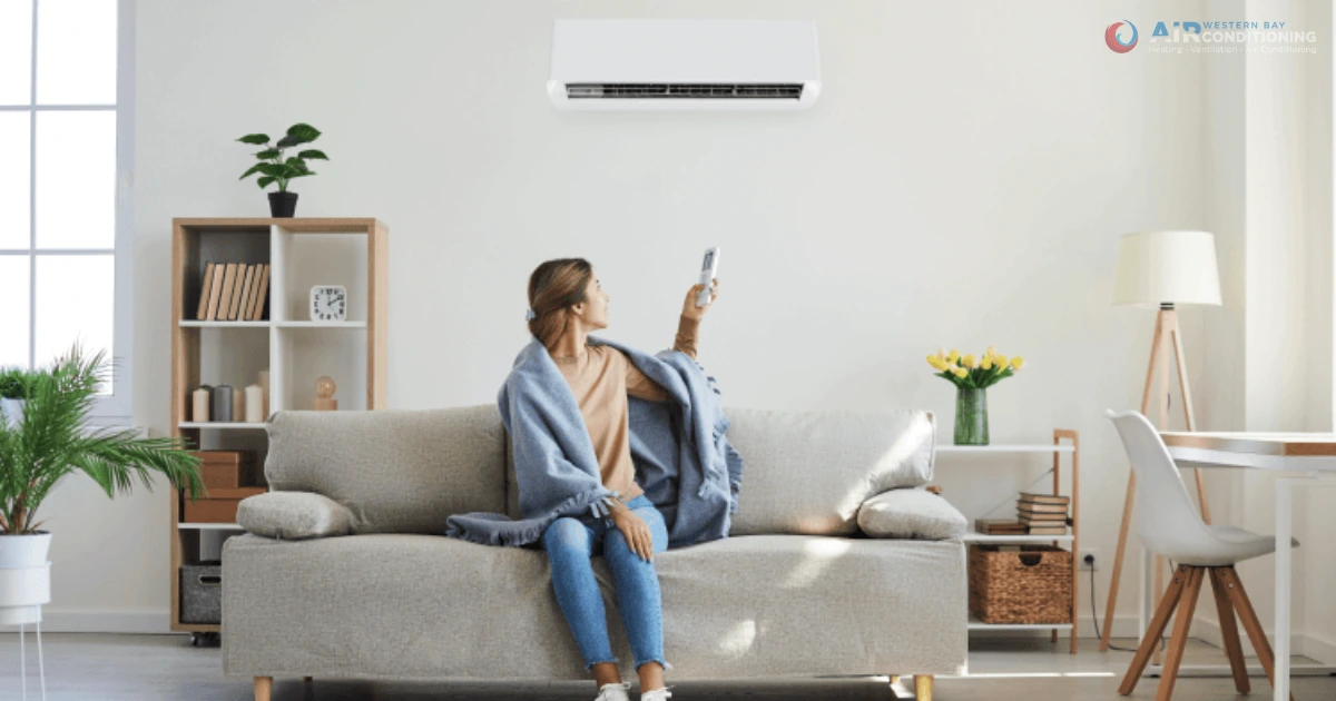 Woman sitting on sofa using remote to operate wall-mounted air conditioner.