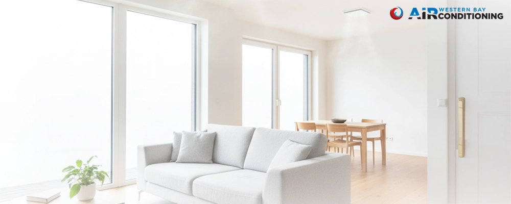 A bright, modern living room featuring a white sofa and a ceiling-mounted ventilation vent dispersing fresh air.