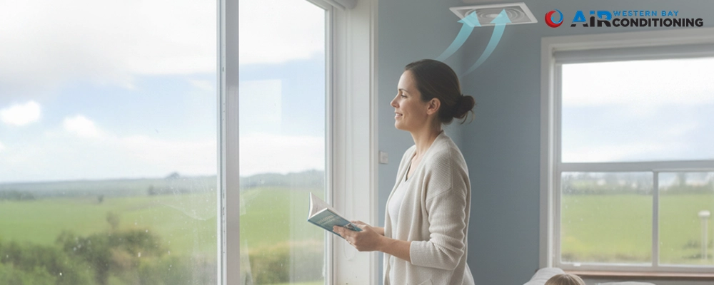 DVS vs HRV ventilation for reducing condensation at home Woman looking at a window while a ceiling vent moves fresh air into the room, showing how DVS vs HRV systems help reduce moisture and condensation.